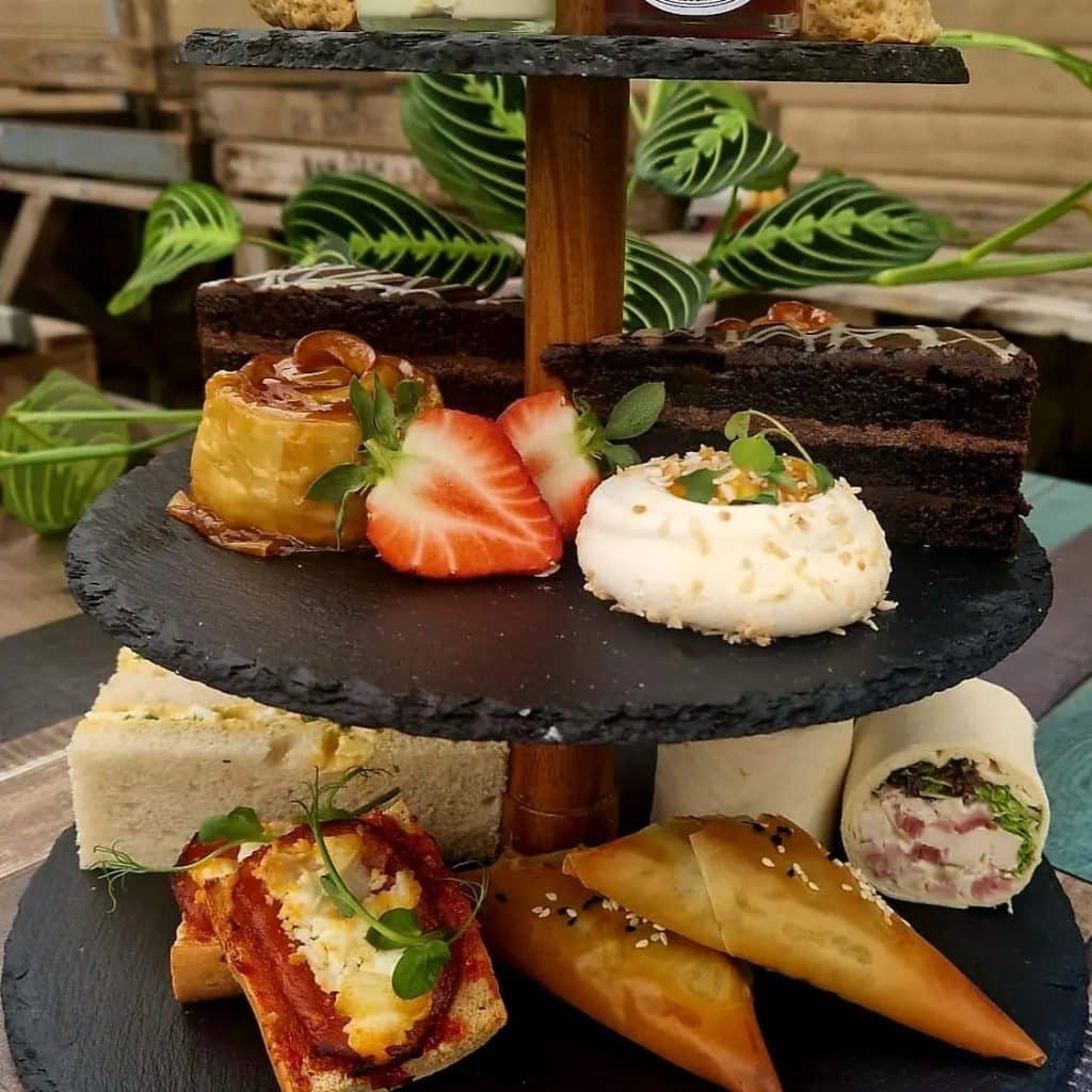 Afternoon Tea On a slate cake stand. With scones, jam, cream, apple roses, coconut & mango meringue, chocolate cake, & delicious sandwiches.